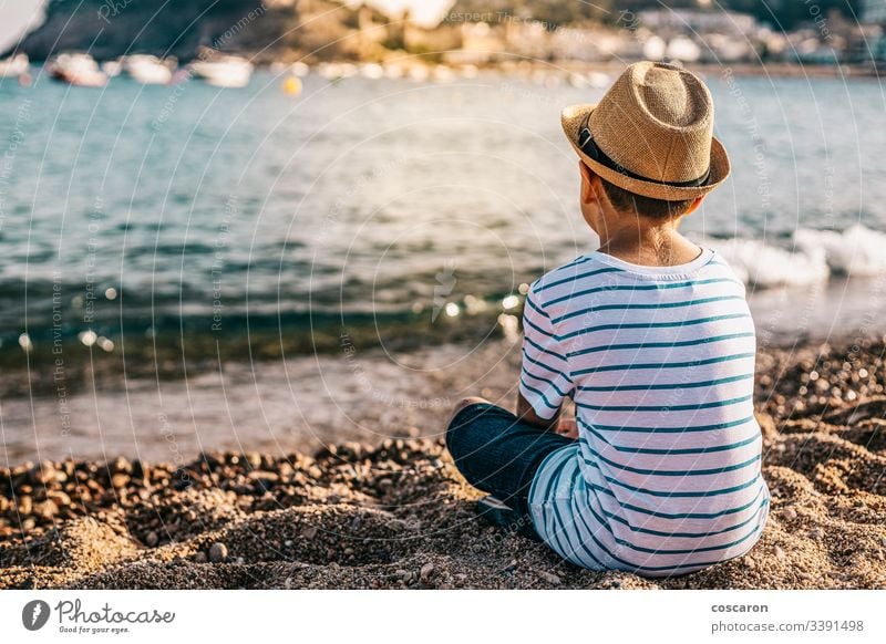 Kleiner Junge mit Hut, der am Strand auf das Meer schaut Rücken Hintergrund schön blau Kind Kindheit Kinder Küste Kontemplation niedlich genießend Mode modisch