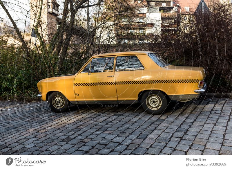 Altes gelbes Auto mit Taxirauten-Beklebung auf einer Kopfsteinpflasterstraße Verkehr Verkehrsmittel Chrom alt Oldtimer Transport Blech Rauten nostalgisch