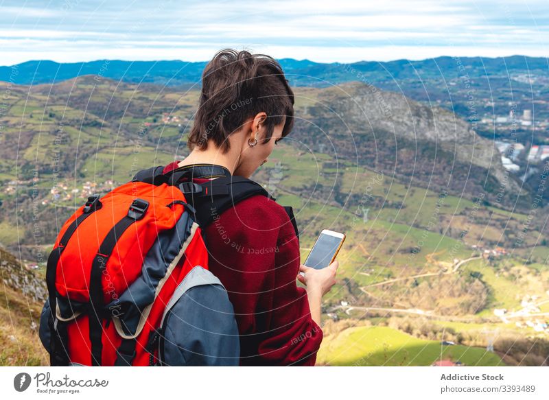 Tourist mit Rucksack und Smartphone wandert auf Bergstraße unter bewölktem Himmel in Spanien Frau Straße Wanderung Trekking Tourismus Abenteuer Hügel Fußweg