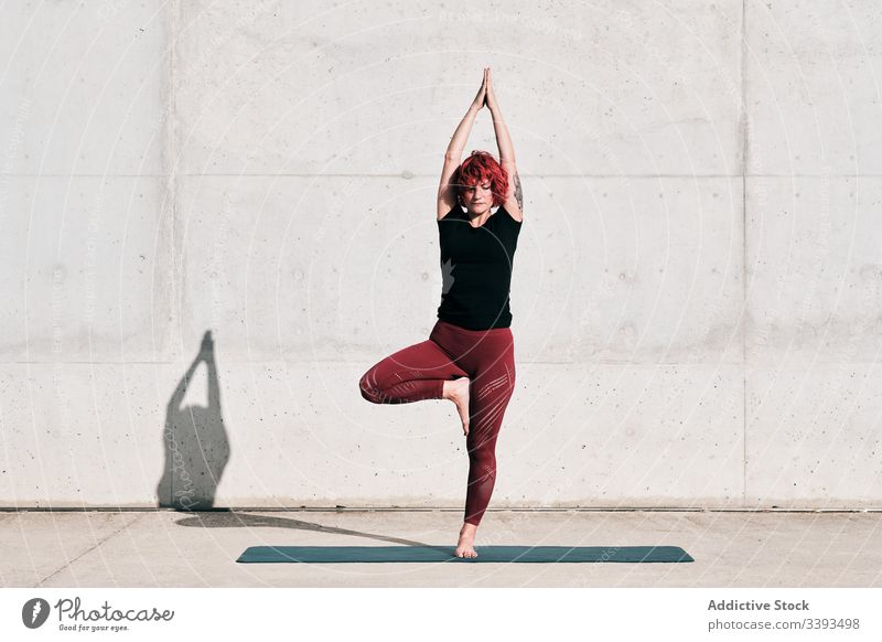 Frau macht Gleichgewichtsübung in Baumhaltung während sie Yoga auf der Straße praktiziert Athlet Namaste meditieren üben Training Übung Dehnung Barfuß Beton