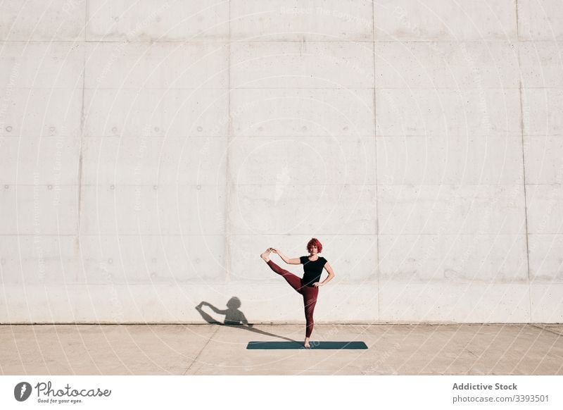 Frau macht auf der Straße eine Yoga-Pose mit ausgestreckter Hand und großem Zeh Dehnung üben Asana Training Übung beweglich Athlet Windstille gymnastisch Beton