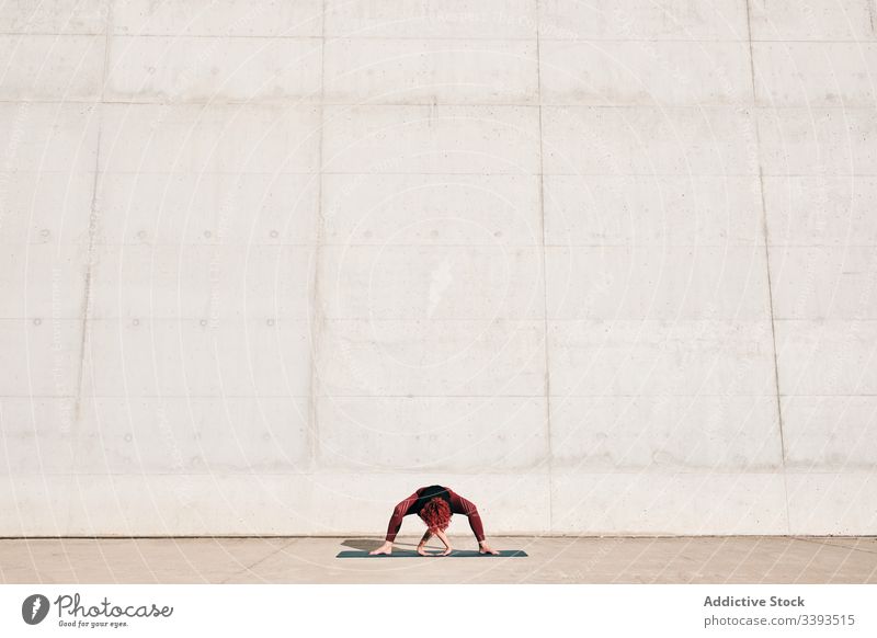 Frau, die auf der Straße eine weitbeinige Vorwärtsbeuge-Yoga-Pose macht Dehnung üben Asana Training Übung beweglich Athlet Windstille gymnastisch Beton urban