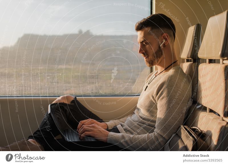 Konzentrierter männlicher Passagier mit Laptop im Zug benutzend Mann Drahtlos Kopfhörer Tippen Reise U-Bahn sonnig Mitteilung Anschluss Kontakt Information
