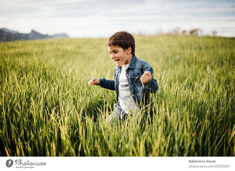 Glücklicher Junge genießt grüne Wiese auf dem Land Feld Landschaft laufen Gras Spaß spielerisch genießen hoch ländlich Freiheit wolkig Spaziergang Kind Natur