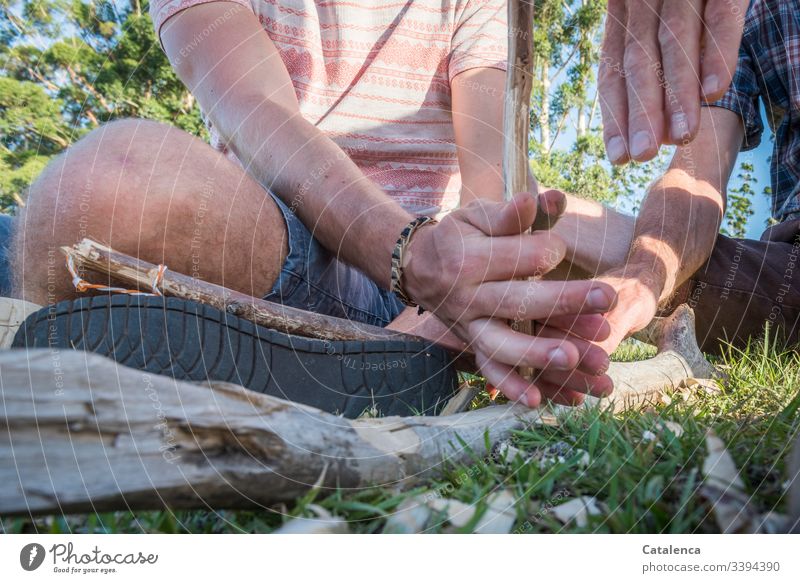 Versuch ein Feuer zu entfachen mit den bloßen Händen, Holz als Unterlage und einem Stöckchen holzstöckchen Hand Detailaufnahme greifen Schuhsole Sommer Gras