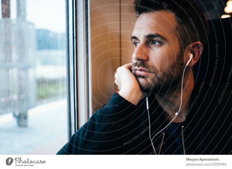 Junger Mann im Zug mit Kopfhörern 30s Erwachsener allein bärtig lässig Kaukasier Arbeitsweg Pendler Tag täglich Typ gutaussehend Reise Leben Lifestyle hören