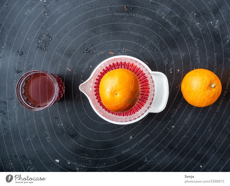 Eine Orange, eine Saftpresse und ein Trinkglas mit Blutorangensaft in einer Reihe auf einem schwarzen Hintergrund, Ansicht von oben saftpresse frischgepresst