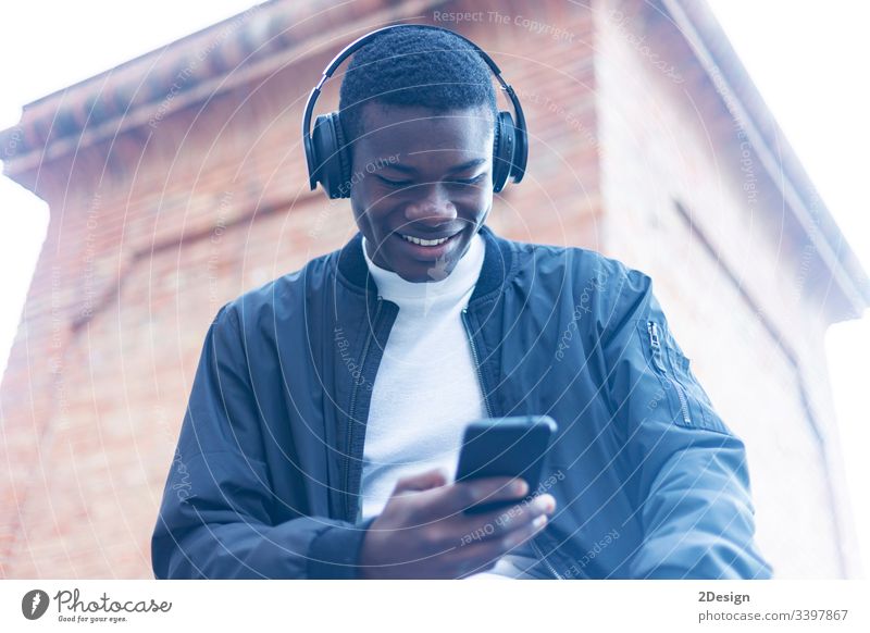 Junger schwarzer Mann steht auf der Straße und hört Musik über Kopfhörer Technik & Technologie Lifestyle männlich Freizeitkleidung trendy Glück Afrikanisch