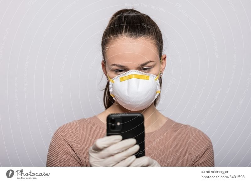 Frau mit Mundschutz und Einmalhandschuhen liest auf dem Smartphone Coronavirus COVID-19 Virus Krankheit Pandemie Epidemie Maske Schützen Handschutz Steril