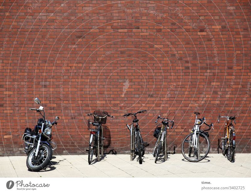 Parkraummanagement ::: fünf Fahrräder und ein Kraftbolzen sonnen sich an einer langweiligen roten Backsteinwand backsteinwand fahrrad parkplatz motorrad sonnig