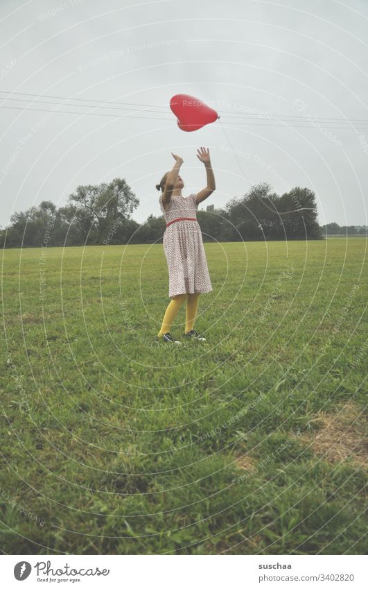 mädchen auf einer wiese, das mit einem roten luftballon in herzform spielt Kind Wiese Natur Gras spielen Luftballon herzförmig Herzform Mädchen Kindheit Sommer