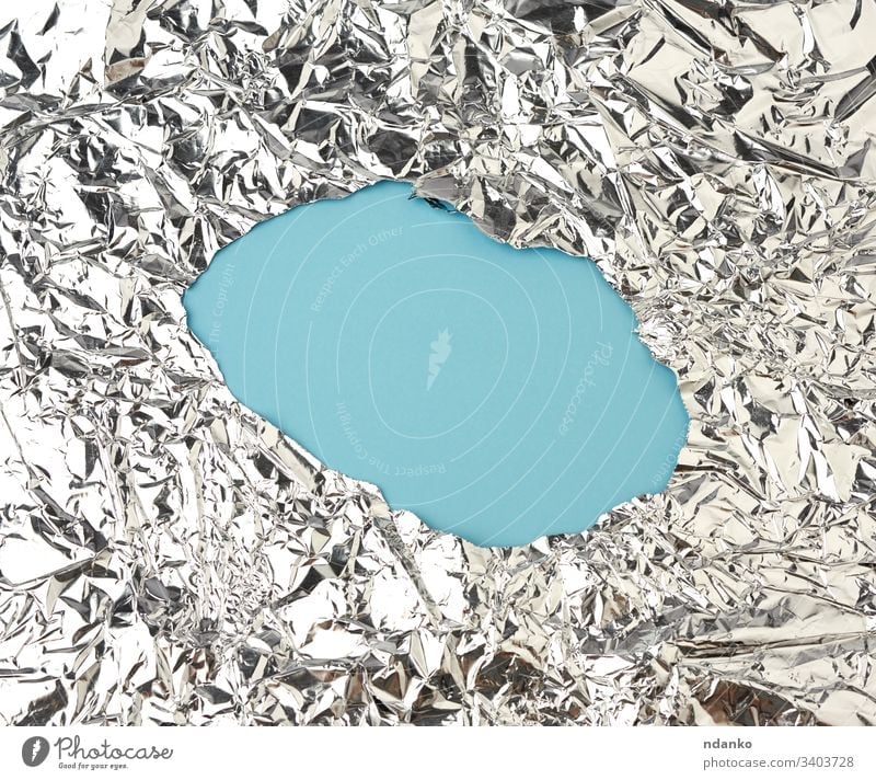 Textur eines glänzenden, zerknitterten Folienstücks mit einem Loch in der Mitte, Verpackungsmaterial für Lebensmittel gefaltet Glanz grau Grunge Golfloch