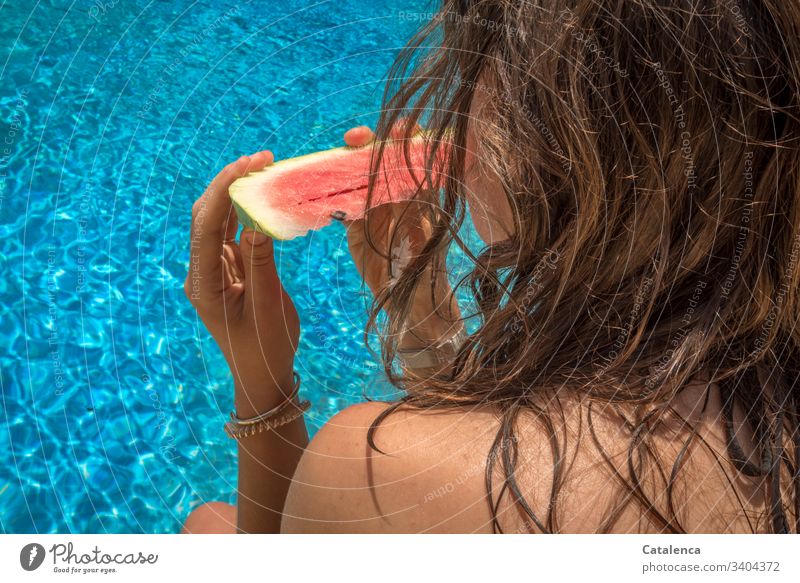 Die braunhaarige junge Frau hält eine Wassermelonenscheibe in Händen während sie auf das blaue Wasser schaut Junge Frau Essen Pool Frucht Sommer Gesundheit