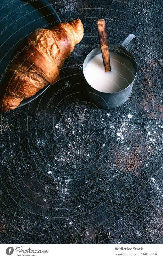 Croissant und Milch auf dem Tisch melken Frühstück Morgen rustikal Becher frisch Lebensmittel Küche Gebäck Brötchen rau unordentlich dreckig selbstgemacht