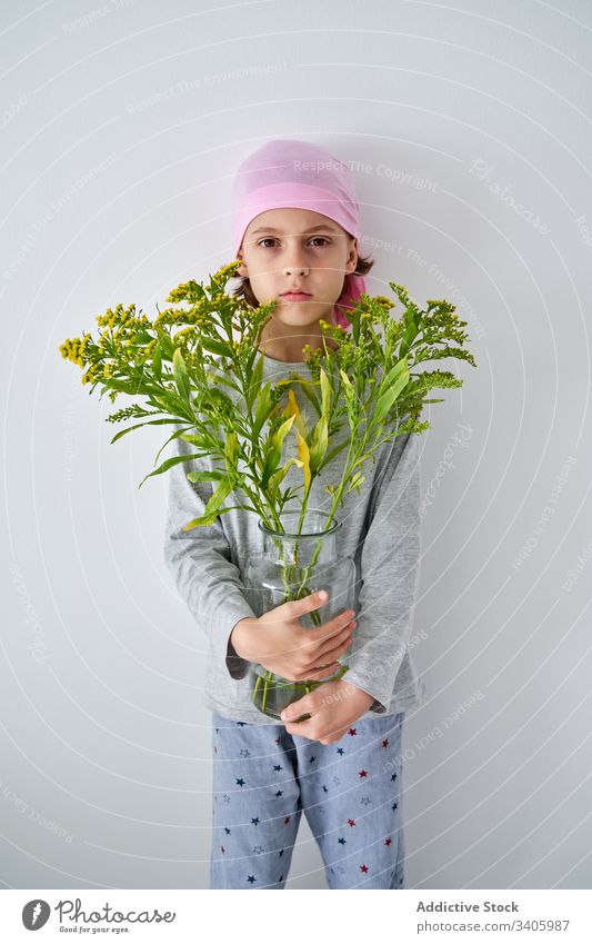 Ernsthaftes niedliches Kind mit Blumen an der Wand Krebs Diagnostik Vase Pflanze Junge krank kämpfen klein männlich geduldig mutig Krankheit gegen Erkenntnis
