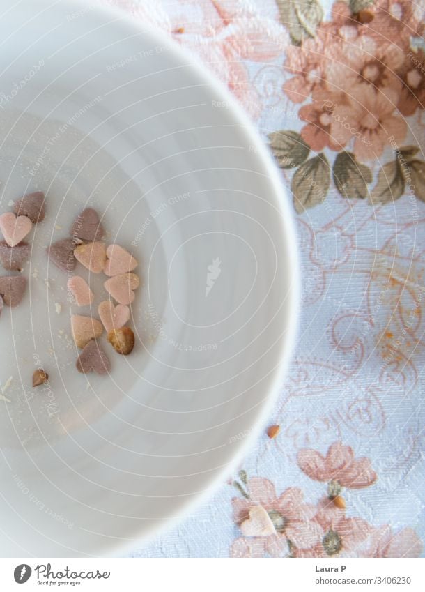 Herzbonbons in einer weißen, runden Schüssel, auf einer alten Tischdecke Süßigkeiten Herzen herzförmig rosa purpur schäbiger Chic altehrwürdig geblümt Blumen