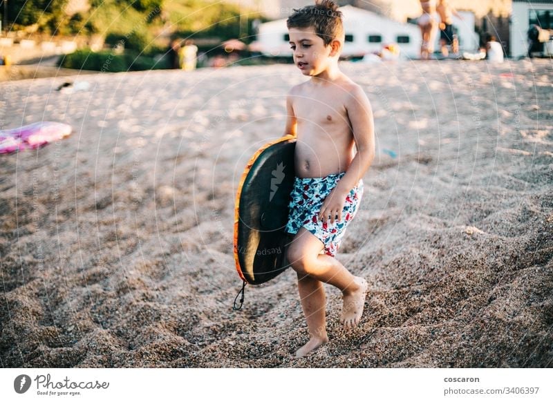 Kleiner Junge mit einem Surfbrett am Strand aktiv Holzplatte Kaukasier Kind Kindheit Küste farbenfroh niedlich genießend Spaß Fröhlichkeit Glück Freude Milan