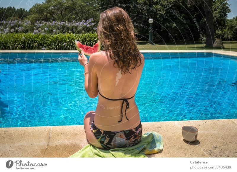 Die Junge Frau mit den nassen Haaren am Rand des Pools verzehrt eine Wassermelonenscheibe Nahrung Ernährung Sommer Schwimmbecken Lebensmittel