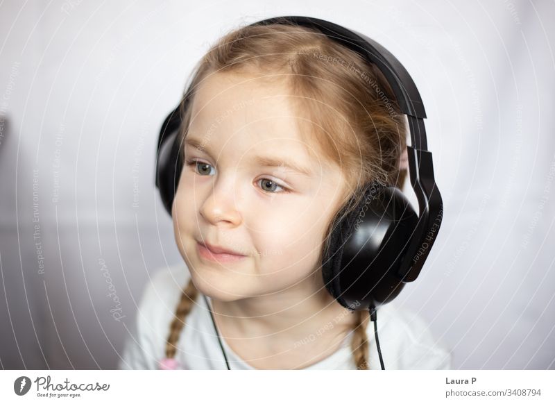 Nahaufnahme eines schönen blonden kleinen Mädchens, das über Kopfhörer Musik hört Lächeln Glück jung Schönheit Kind wenig Tochter Spaß niedlich genießen