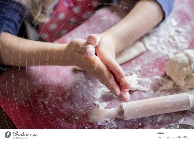 Nahaufnahme von Kinderhänden neben einem Nudelholz, die mit dem Teig spielen wüst Vorbereitung roh Küche bezaubernd niedlich süß abschließen wenig backen