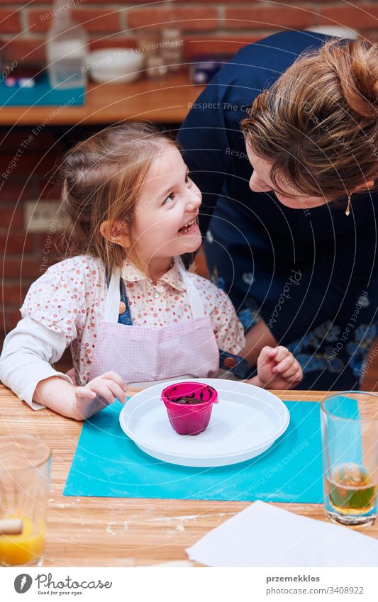 Glückliches, zufriedenes kleines Mädchen, das den selbstgemachten Muffin genießt. Teilnahme am Backworkshop. Backkurse für Kinder, aufstrebende kleine Köche. Kochen lernen. Kombinieren und Rühren von zubereiteten Zutaten. Echte Menschen, authentische Situationen