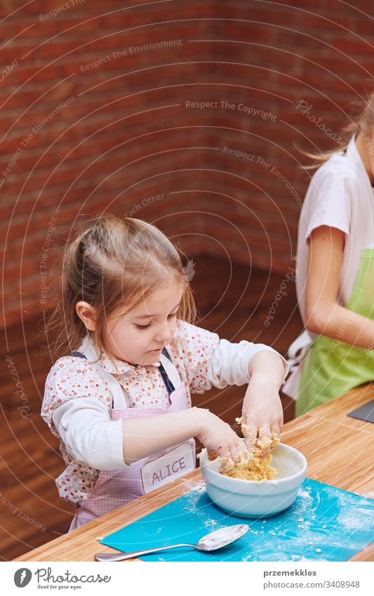 Kleine Mädchen kneten den Teig für den Kuchen. Kinder, die am Backworkshop teilnehmen. Backkurse für Kinder, aufstrebende kleine Köche. Kochen lernen. Kombinieren und Rühren von vorbereiteten Zutaten. Echte Menschen, authentische Situationen