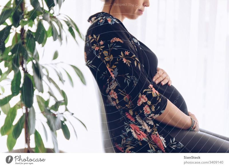 Hübsche junge schwangere Frau am Fenster sitzend Schwangerschaft schön Bauch Glück Leben heimwärts Mutterschaft Pflege Baby Konzept Pflanzen Erwartung Unterleib