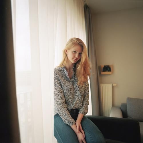 Portrait einer jungen Frau neben dem Fenster an der Gardine Mädchen blond schön schlank anmutig elegant lifestyle Wohnen Wohnung zu Hause Bluse Muster