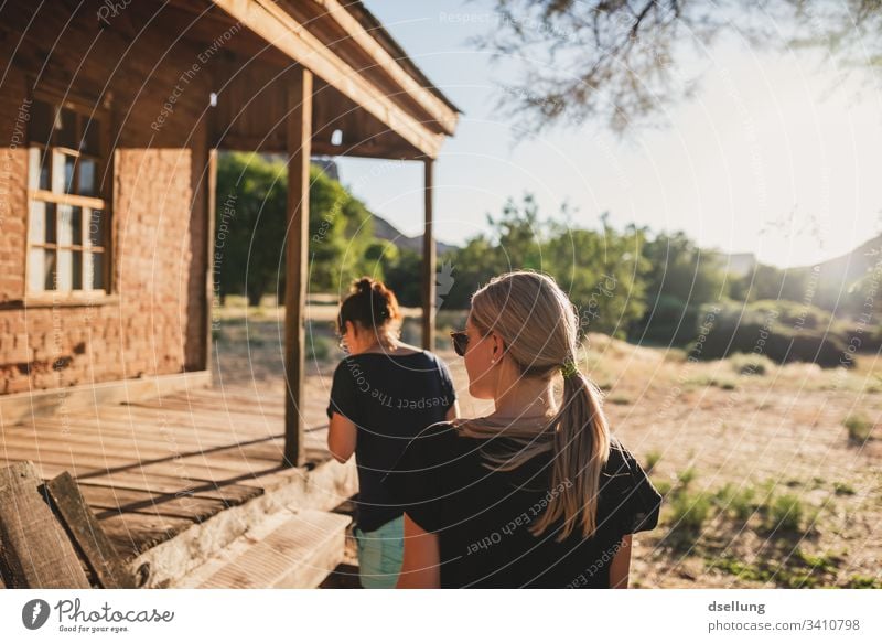 Zwei junge Frauen gehen im Abendlicht auf ein Holzhaus zu genießen erholen entspannen zielstrebig zuversicht Zukunft Blick nach vorn natürlich Bäume Pflanze