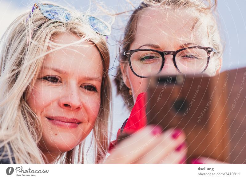 Zwei junge Frauen schauen gemeinsam auf ein Smartphone Brillenträger Leichtigkeit entspannt Lebensfreude selbstbewußt Lächeln Zufriedenheit aufmerksam lächeln