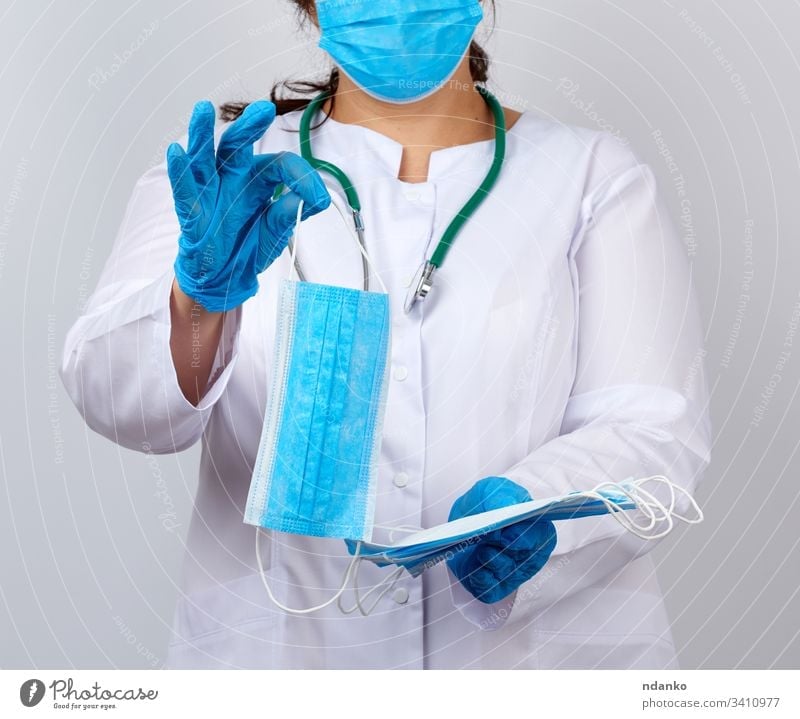 Ärztin im weißen Kittel und mit Maske hält einen Stapel schützender Gesichtsmasken über das Virus Erwachsener Assistent blau Pflege Kaukasier Klinik klinisch