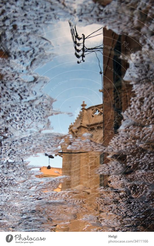 Teil einer Kirche spiegelt sich in einer Pfütze Spiegelung Gebäude Gebäudeteil Gemäuer Kreuz alt historisch Stein Gehweg Wasser Himmel Reflexion surreal