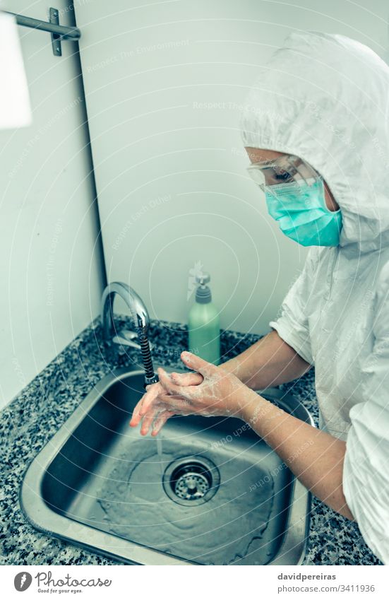 Frau im bakteriologischen Schutzanzug beim Händewaschen Hände waschen Seuche COVID19 Prävention Hygiene desinfizieren Krankenhaus Seifenspender Reibung Virus