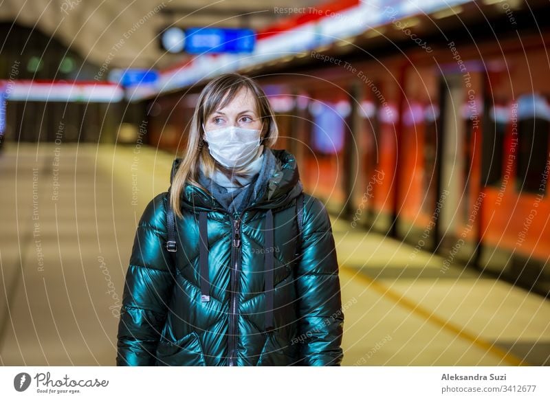 Frau im Wintermantel mit Schutzmaske auf dem Gesicht in der U-Bahn-Station stehend, auf den Zug wartend und besorgt schauend. Präventivmaßnahmen an öffentlichen Plätzen von Epidemiegebieten. Finnland, Espoo