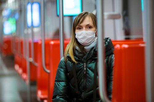 Frau im Wintermantel mit Schutzmaske auf dem Gesicht steht im U-Bahn-Wagen, telefoniert und sieht besorgt aus. Präventivmassnahmen an öffentlichen Orten von Epidemiegebieten. Finnland, Espoo