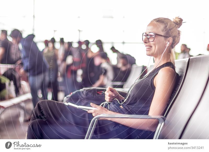 Eine weibliche Reisende, die ihr Handy benutzt, während sie an den Abfluggates des asiatischen Flughafenterminals auf das Einsteigen in ein Flugzeug wartet.
