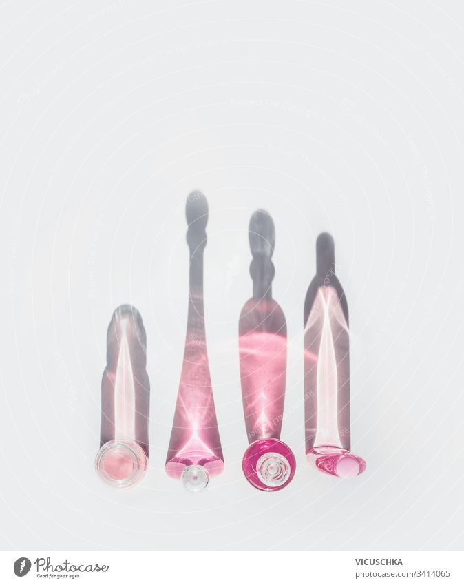 Moderne rosafarbene Kosmetikflaschen für die Hautpflege im Sonnenlicht mit langem Schatten auf weißem Schreibtisch. Ansicht von oben. Hautpflege für das Gesicht. Anti-Aging-Schönheitskonzept