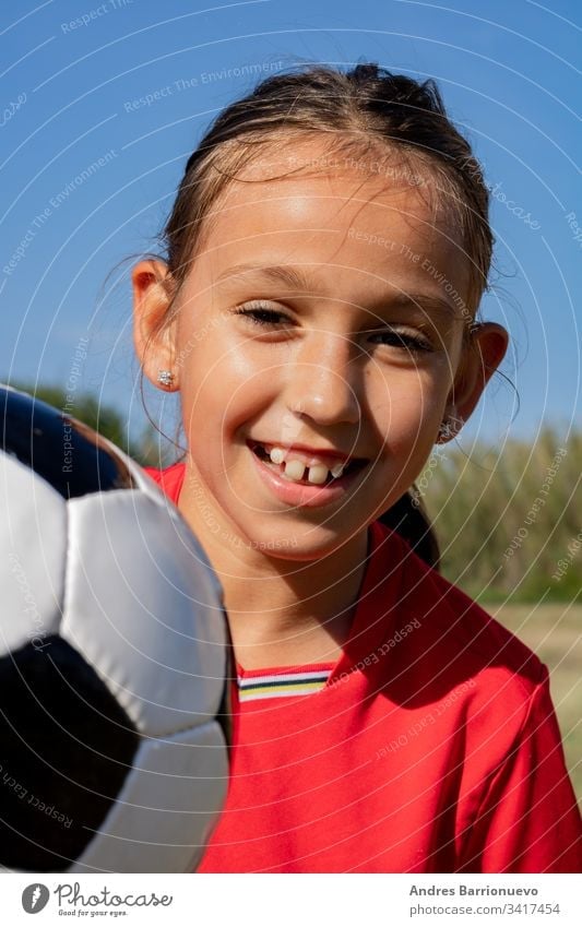 Kleines Mädchen spielt Kind wenig Fußball Jugend Lächeln außerhalb Ball jung Gras Kinder Hände auf den Hüften vertikal im Freien Selektiver Fokus Uniform grün