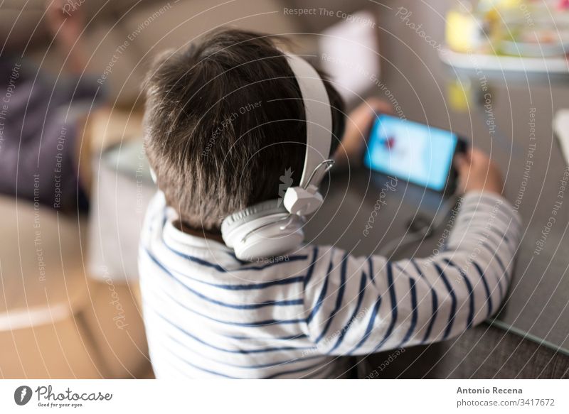 Junge zu Hause, der mit Kopfhörern auf das Telefon schaut Kind Smartphone Technik & Technologie Sucht unsachgemäß 3-4 Jahre alt 4-5 Jahre alt heimwärts