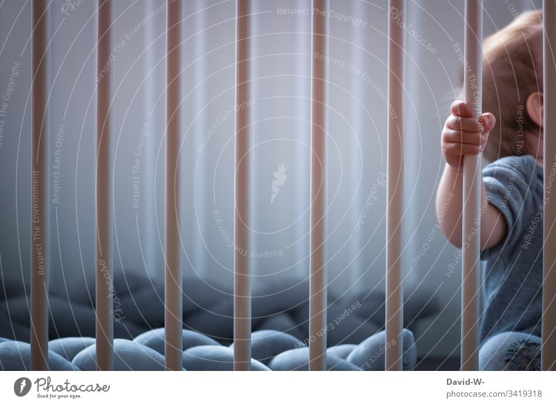 Baby im Kinderbett umklammert das Gitter Gitterbett Bettchen Stangen Stäbe eingesperrt anonym Kleinkind niedlich allein Verantwortung Kindererziehung Familie