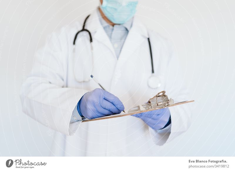 Arzt mit Schutzmaske und Handschuhen im Haus. Schreiben von Notizen auf einer Mappe. Konzept des Coronavirus Mann professionell Corona-Virus Krankenhaus