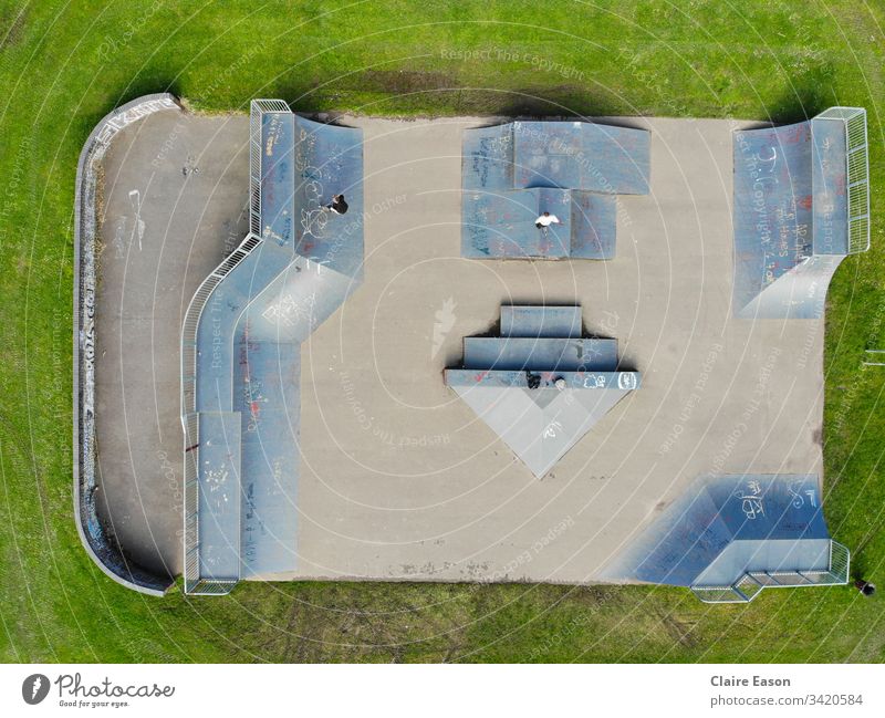 Luftaufnahme eines Skateparks mit 2 nicht identifizierbaren Jugendlichen. Grau-blaue Rampen vor einem Grashintergrund. erstellt von dji camera Skateboarding