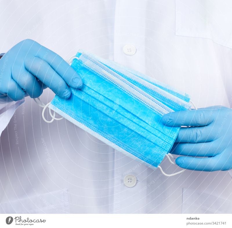 Arzt in weißem Kittel, blaue sterile Latexhandschuhe halten textile medizinische Masken in der Hand Mundschutz Sanitäter Medizin Krankenpfleger Beruf geduldig
