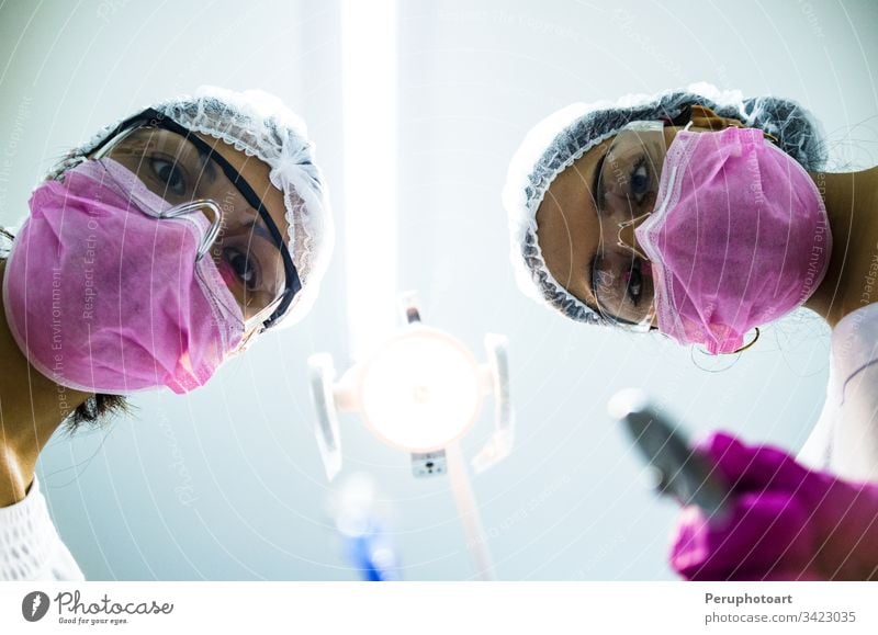 Unteransicht von zwei Zahnärztinnen mit chirurgischer Maske, die Werkzeuge halten und in die Kamera schauen dental Mundschutz Operation Frauen Zahnarztpraxis