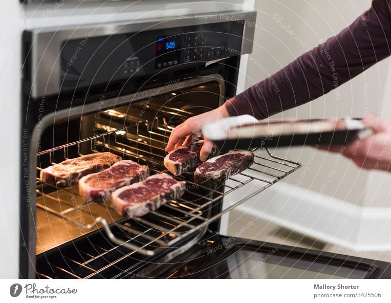 Mann schiebt Steaks in den Ofen rohes Steak Rindfleisch rohes Rindfleisch Essen zubereiten Kochsteak Mann kocht Kochen von Steaks im Ofen rotes Fleisch