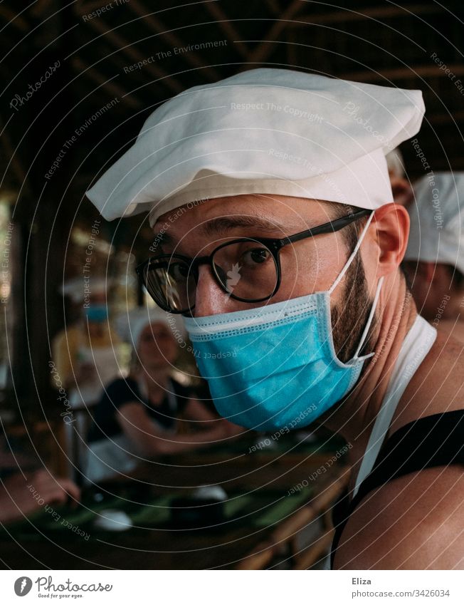 Ein Mann mit Mundschutz und Kochmütze bei einem Kochkurs Corona Virus Maske Gesichtsmaske Mund-Nasen-Maske medizinische Maske Ansteckung covid-19 schützen