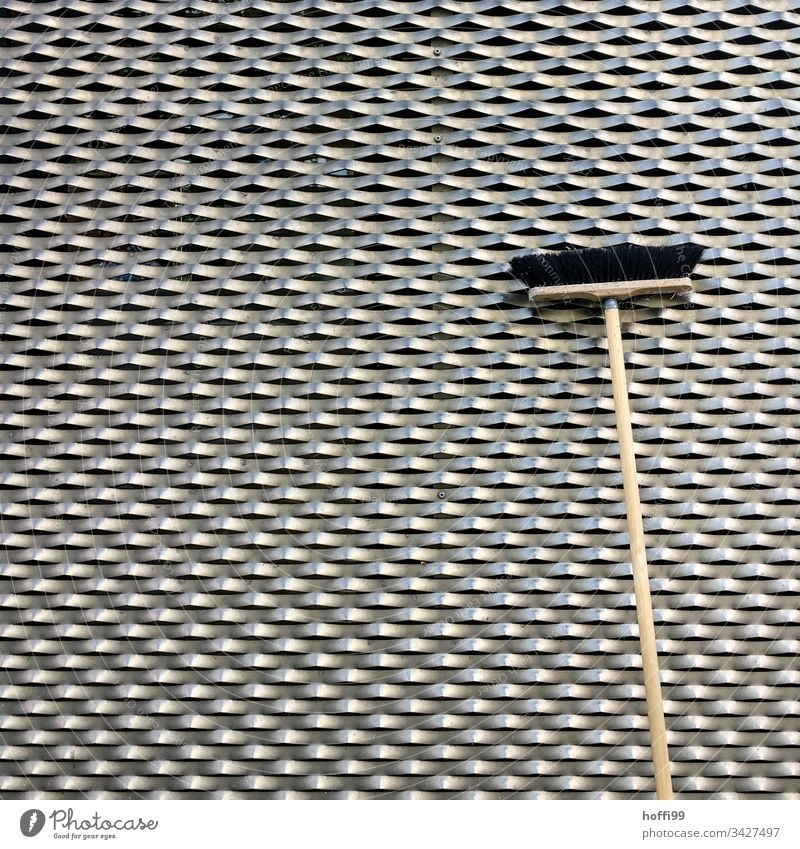 Besen vor einer Metallfassade Besenstiel Besenkammer Strukturen & Formen Verkleidung von Fassaden Architektur Wabenmuster Wellen Silber schwarz Muster
