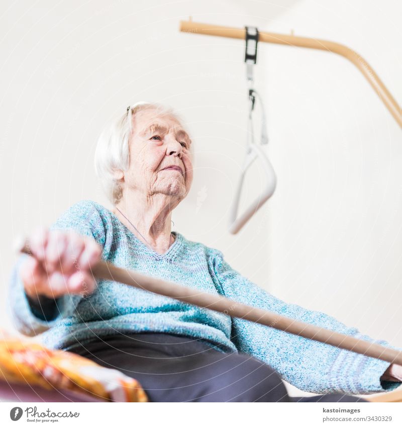 Ältere 96 Jahre alte Frau, die mit einem Stock trainiert, der auf ihrem Körper sitzt. Gesundheitswesen Senior geriatrisch Training Pflege heimwärts Arbeit Bett