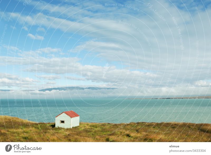 kleine Hütte am Ufer und Blick über das Wasser bis zu wolkenverhangenen Bergen (Island) Reykir einsam Einsamkeit Außenaufnahme Natur Haus Landschaft Wolken