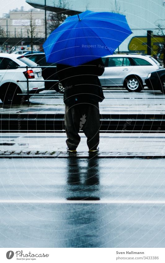 Mann mit blauem Regenschirm wartet Blau regenschirm mann baggy Haltestelle autos warten Mensch Erwachsene schlechtes Wetter Farbfoto Außenaufnahme nass Wasser